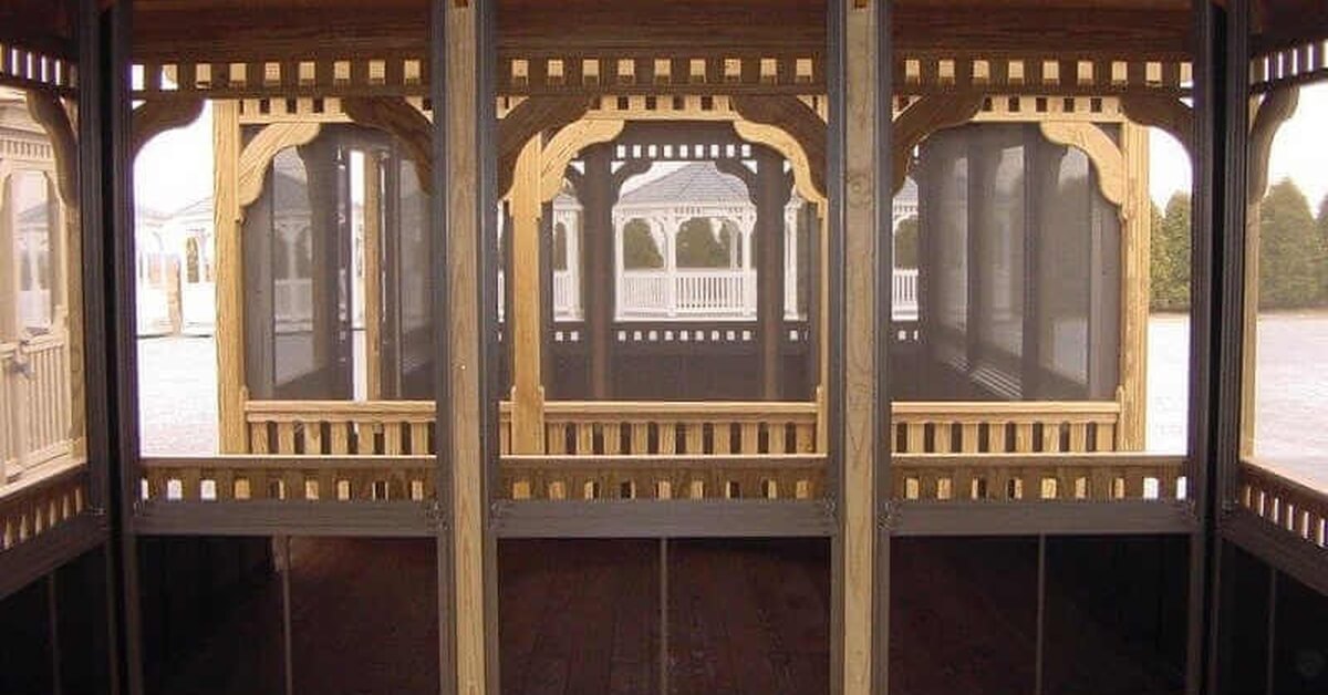 a wooden gazebo interior with screened panels, decorative trim, railing sections, and a plank floor.